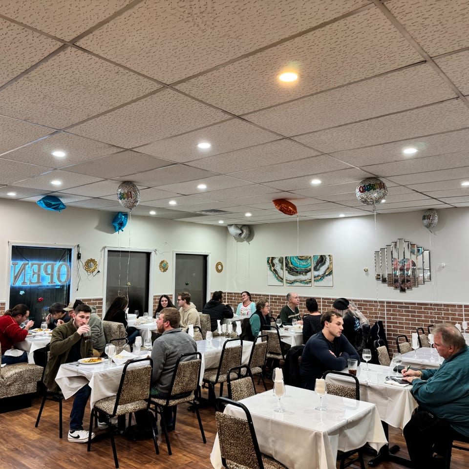 Diners seated at tables with white tablecloths in a brightly lit Indian restaurant with balloons.