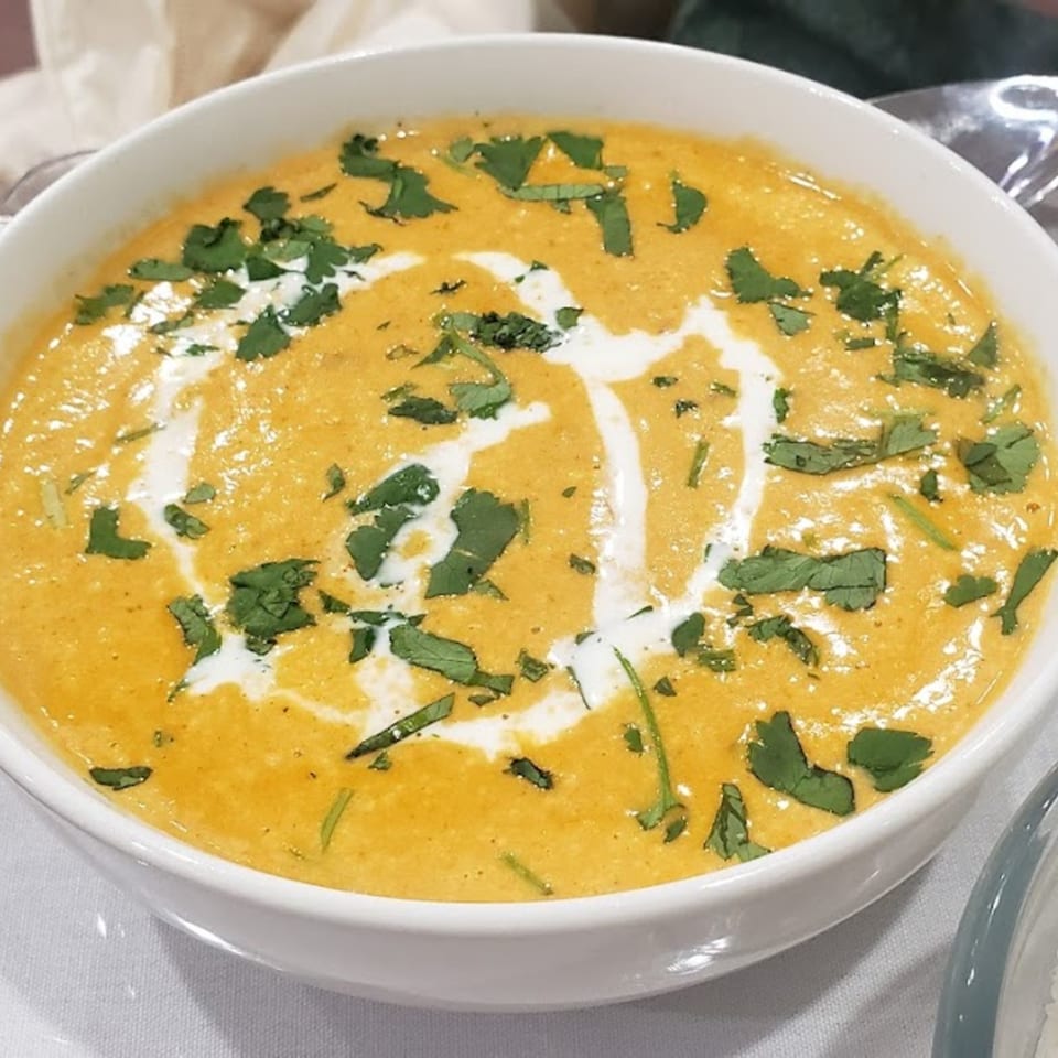 A white bowl filled with creamy orange butter chicken, garnished with fresh cilantro and cream swirls.