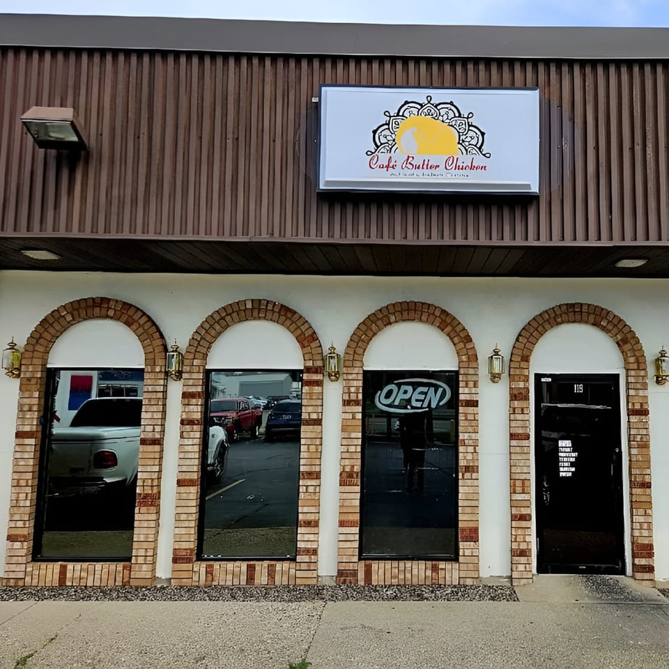Exterior of Café Butter Chicken, an Indian restaurant, with a sign and arched brick windows.