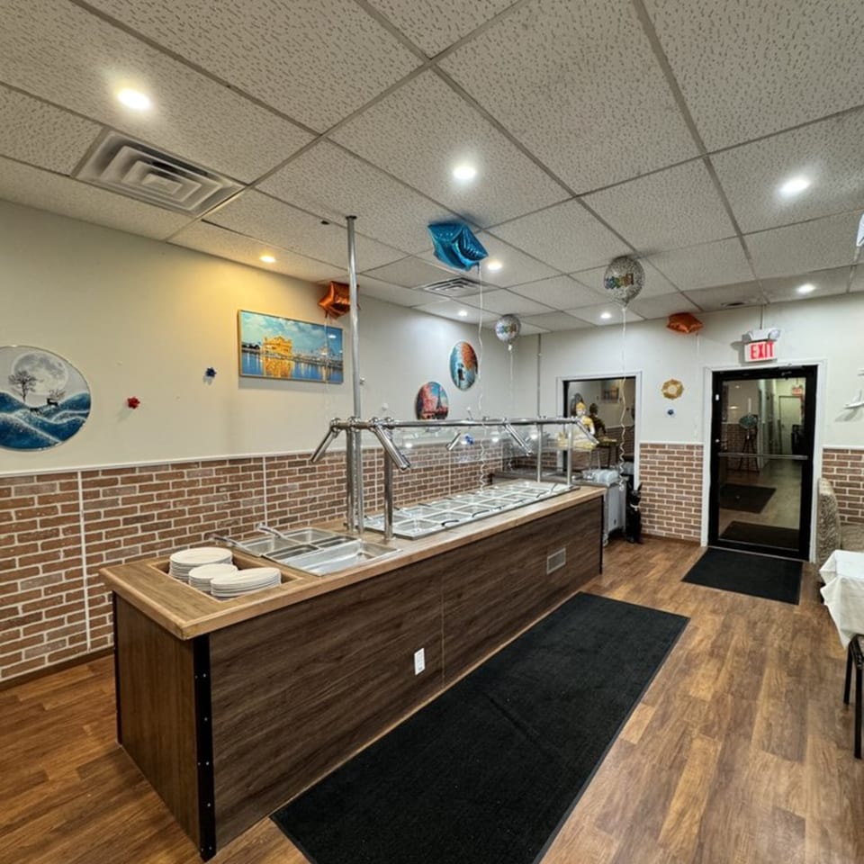 An empty buffet line with stainless steel food warmers and stacked plates inside Café Butter Chicken.