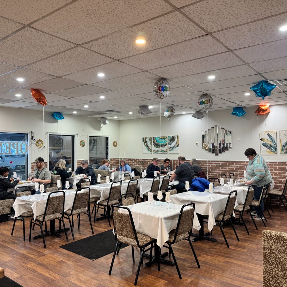 Diners seated at tables in a brightly lit Indian restaurant, with balloons decorating the ceiling.