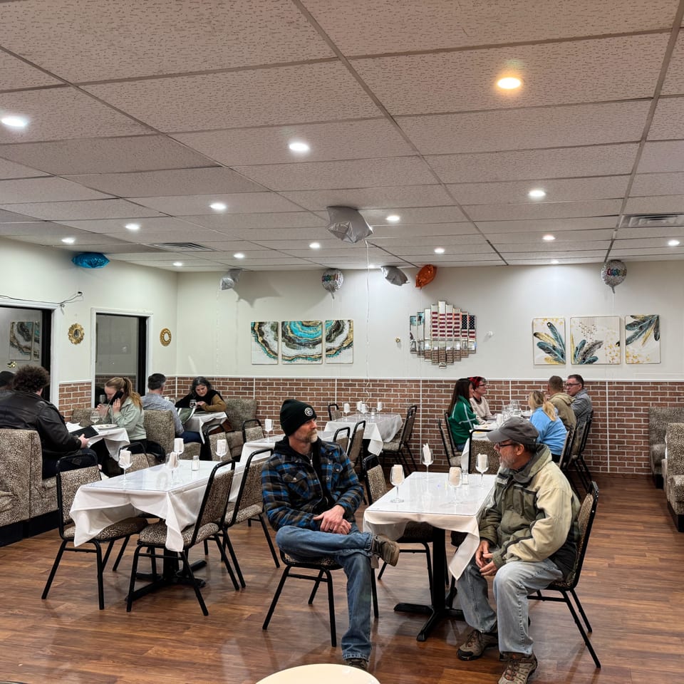 Diners seated at tables with white tablecloths in the Café Butter Chicken restaurant, with brick and art decor.