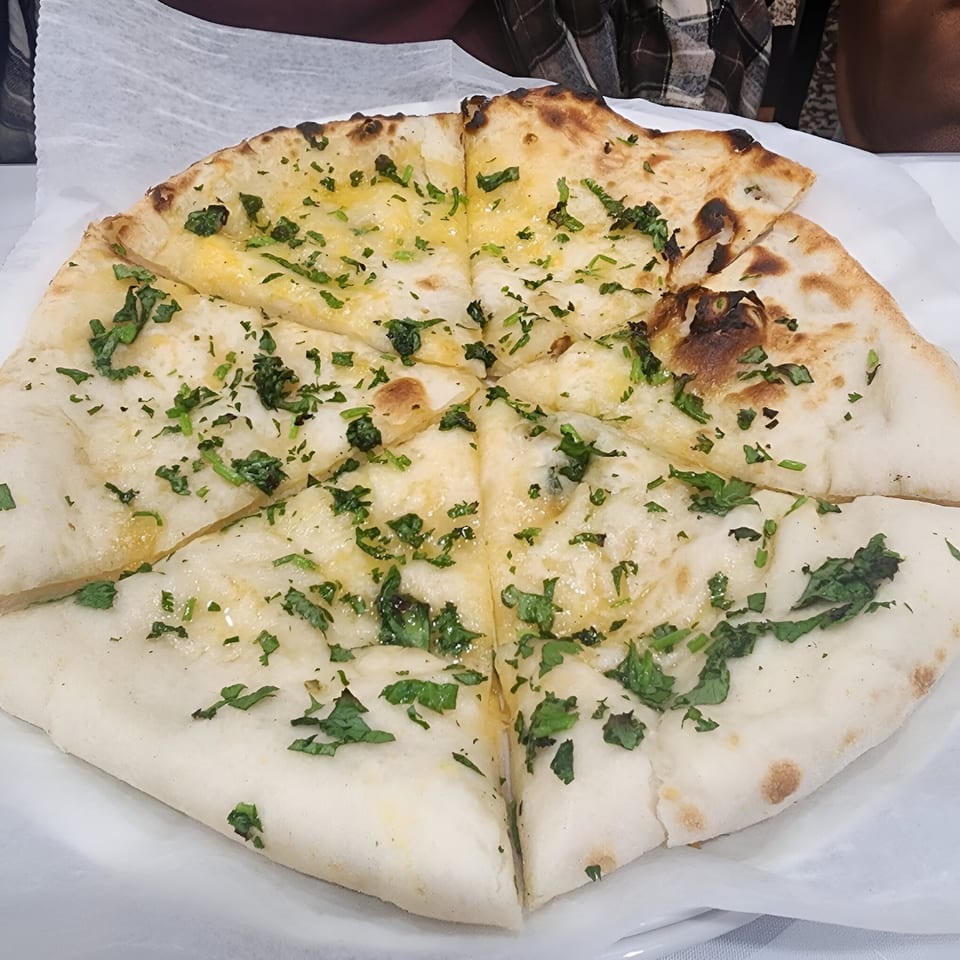 Garlic naan bread, cut into wedges and topped with fresh cilantro, on a white plate.
