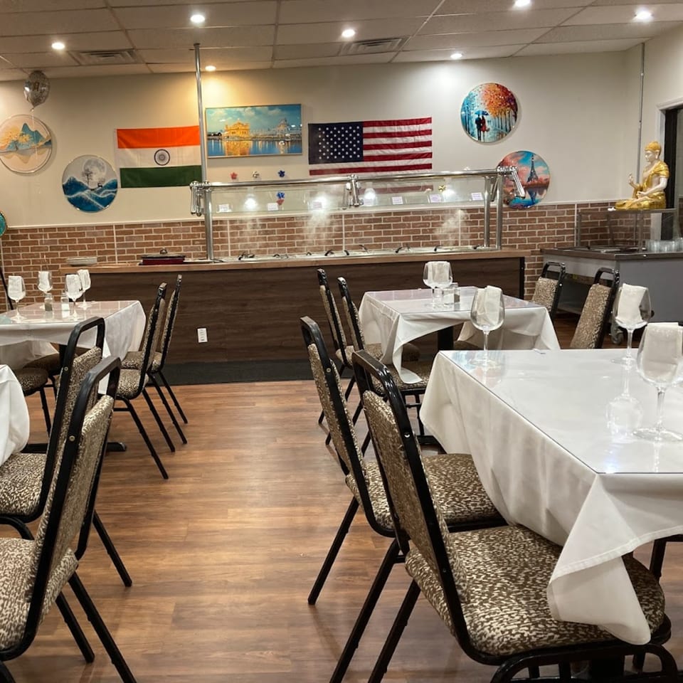 Empty dining room at Café Butter Chicken with buffet, tables set with white cloths, and flags on the wall.