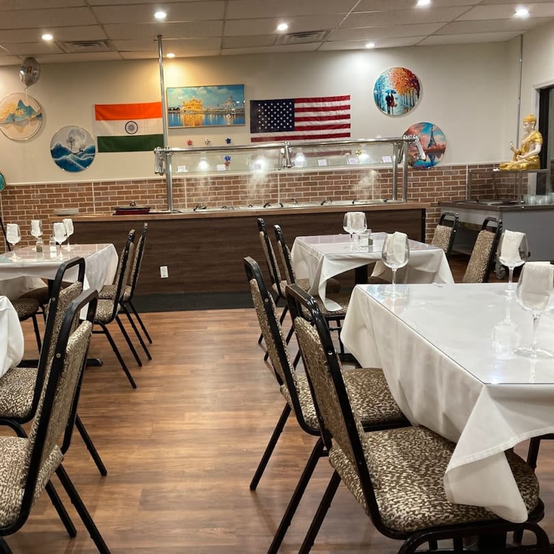 Empty dining room at Café Butter Chicken with buffet, tables set with white cloths, and flags on the wall.