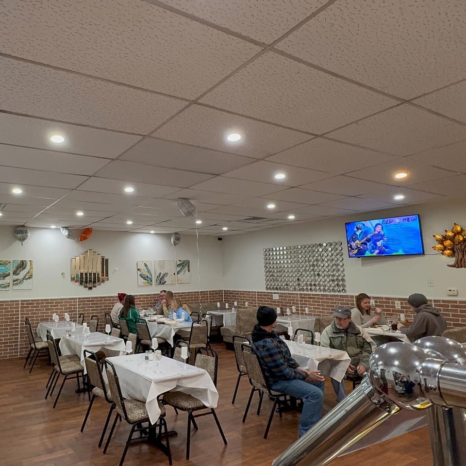 Diners seated at tables in the Café Butter Chicken dining room with brick walls and a TV.