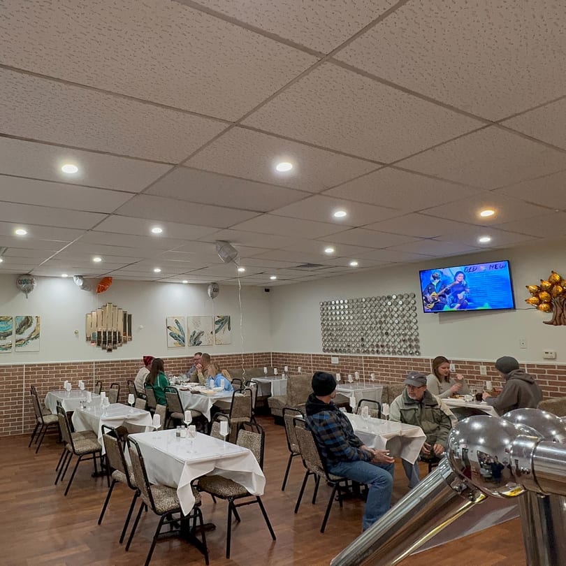 Diners seated at tables in the Café Butter Chicken dining room with brick walls and a TV.
