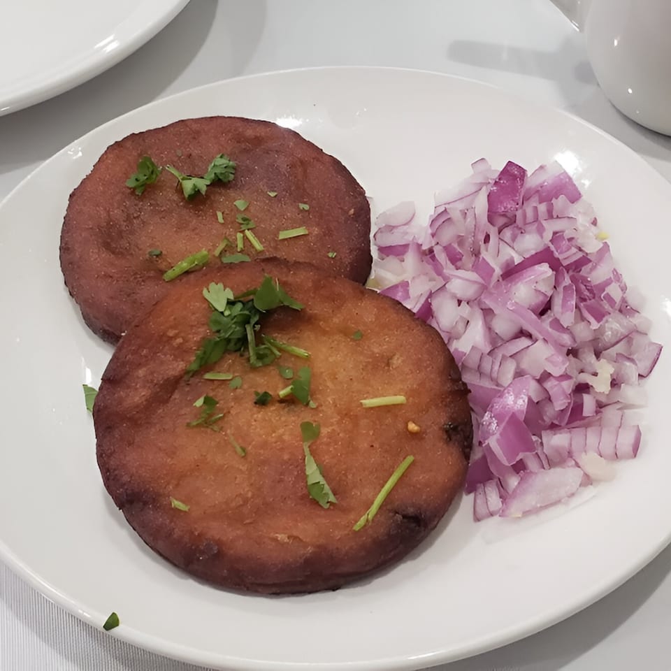Two golden-brown Indian aloo tikki patties with cilantro, served with a side of diced red onions.