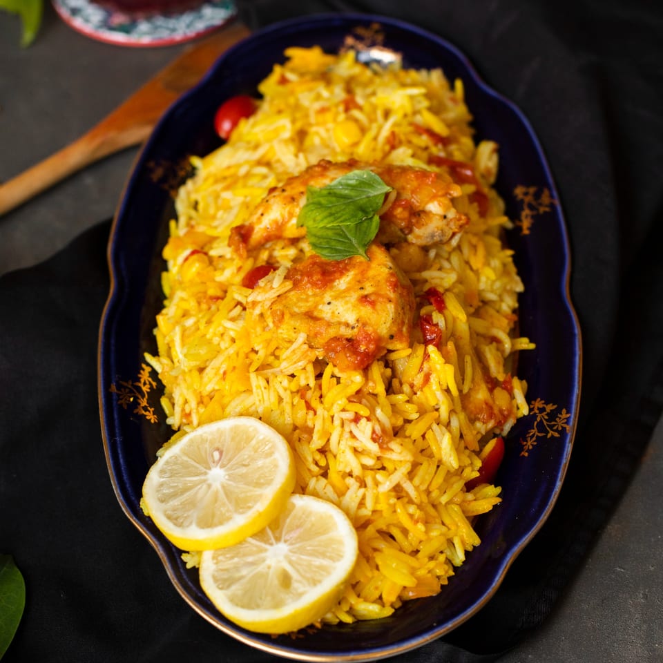 Indian chicken biryani with lemon slices and a mint garnish on a dark blue platter.