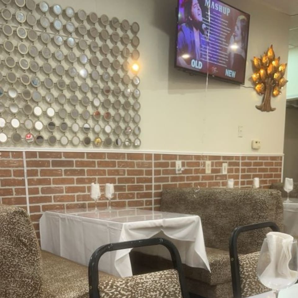 Restaurant interior with brick walls, patterned booths, a TV playing music, and a decorative mirror wall.