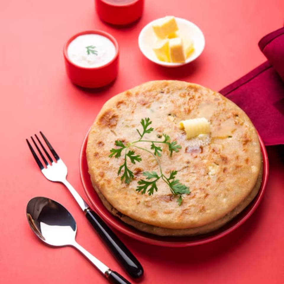 Indian paratha with butter and cilantro, served with yogurt and chutney on a red background.